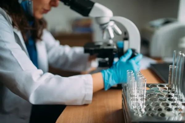 onscherp beeld van een vrouwelijke onderzoekster die door een microscoop kijkt