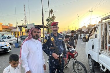 Een Iraakse jongen, man en politieagent poseren op straat in de stad Hawija.
