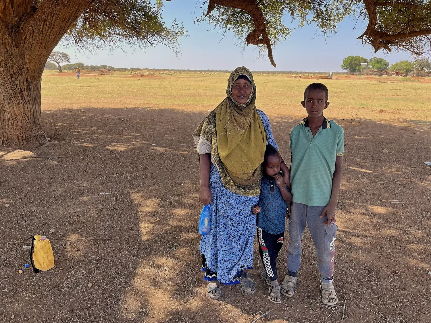 Een oude vrouw poseert samen met twee kleine kinderen in de schaduw van een boom voor de lens van de fotograaf