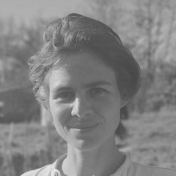 Black and white portrait of a person with short hair, smiling gently, against a blurred outdoor background.