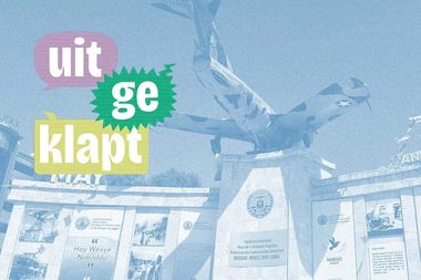 Monument with an airplane statue atop a pedestal, surrounded by informational panels. Colorful text reads "uitgeklapt" to the left.