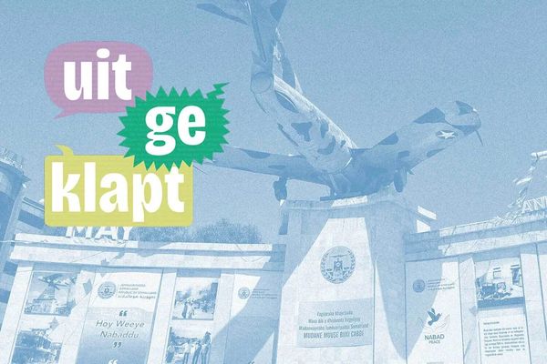 Monument with an airplane statue atop a pedestal, surrounded by informational panels. Colorful text reads "uitgeklapt" to the left.