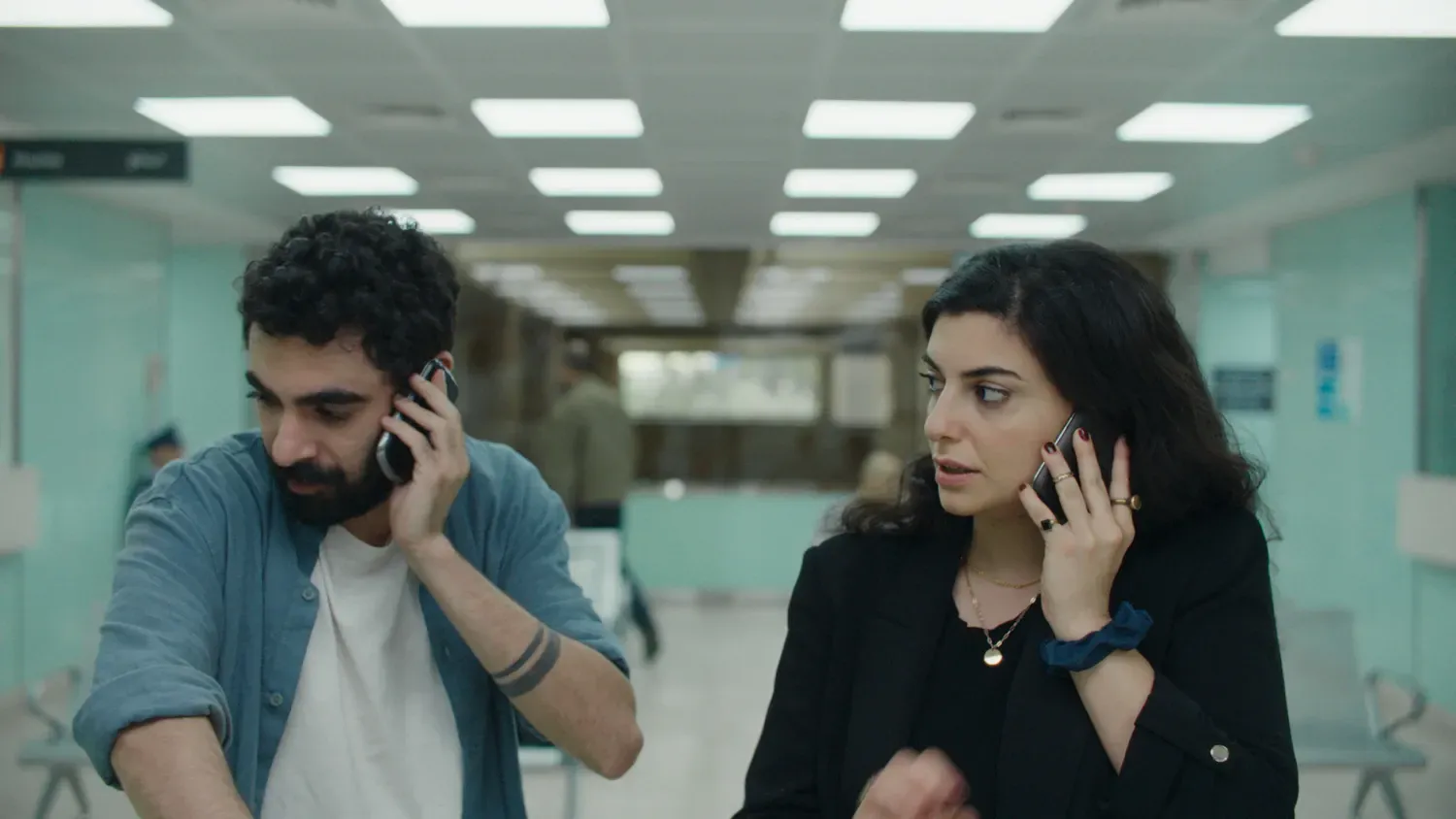 De twee hoofdpersonages uit de film zitten naast elkaar, beide met een telefoon in de hand