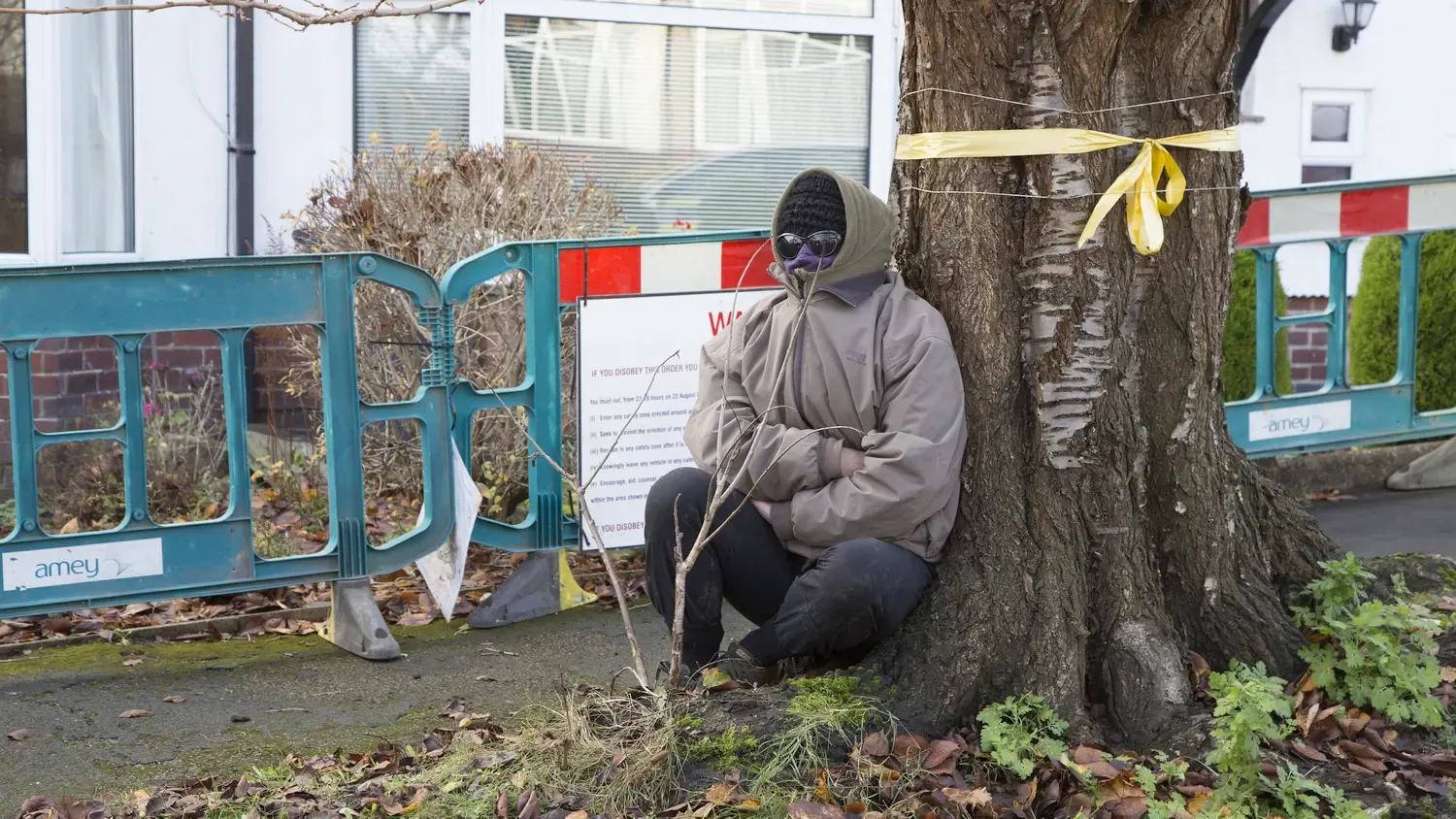 Een gemaskerde man zit voor een boom die gemarkeerd is om te worden gekapt.