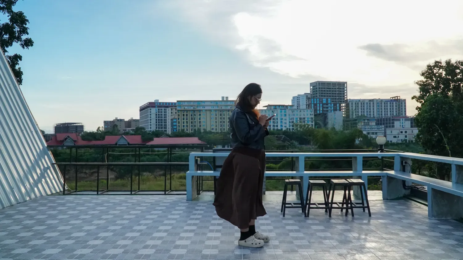 Een vrouw is bezig op haar mobiele telefoon. Op de achtergrond in de verte appartemenstgebouwen.