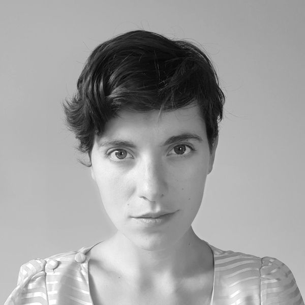 A person with short, brown hair wearing a light, striped blouse, looking directly at the camera against a plain background.