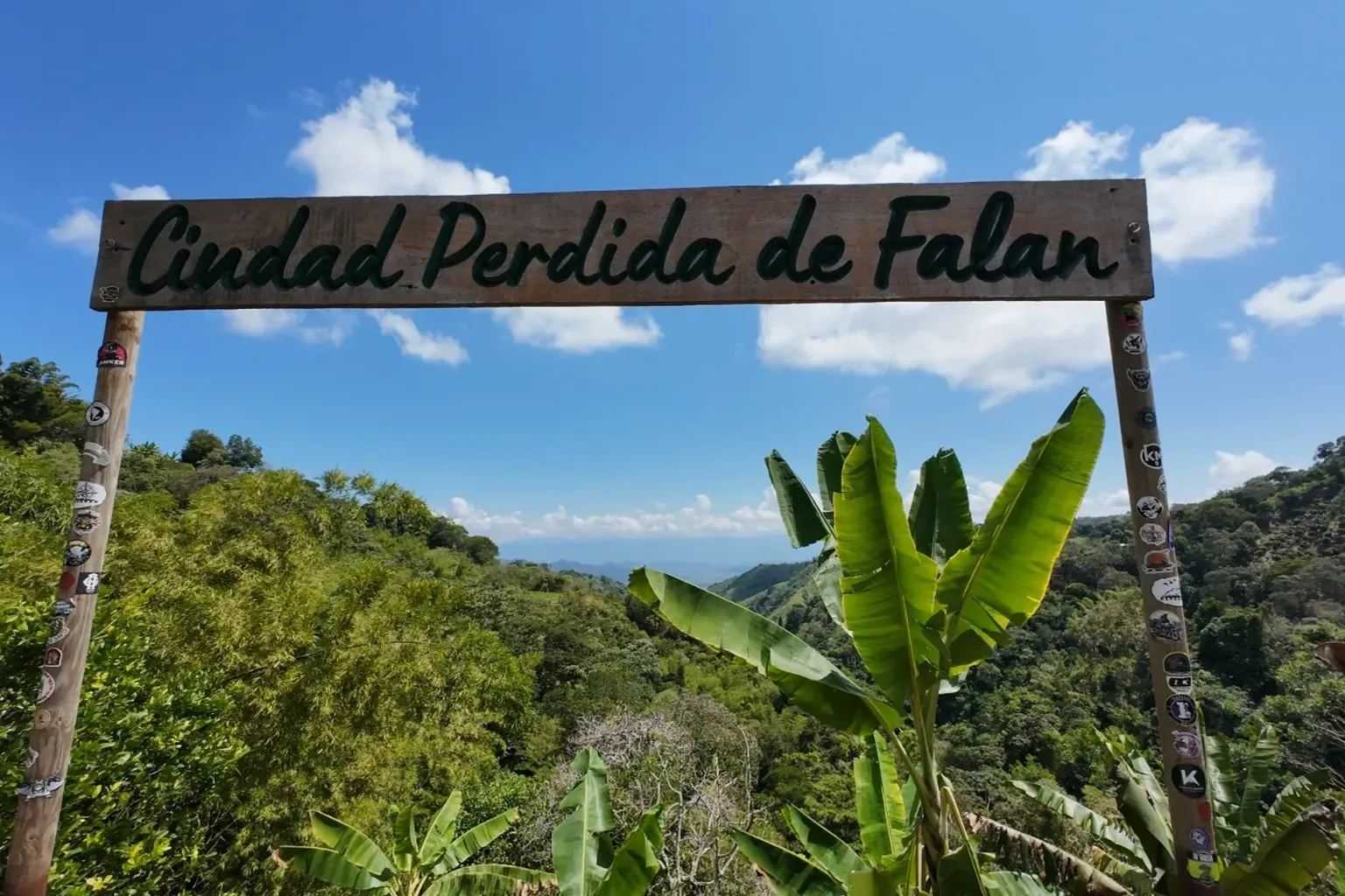 zicht op het bladerdak van een oerwoud. Vooraan een naambord waarop staat ‘Ciudad Perdida de Falan’