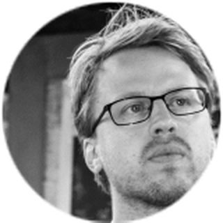 Black and white image of a person with glasses and short hair, looking thoughtfully off to the side.