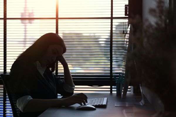 Silhouetted woman in office working on a computer, with sunlight streaming through blinds.