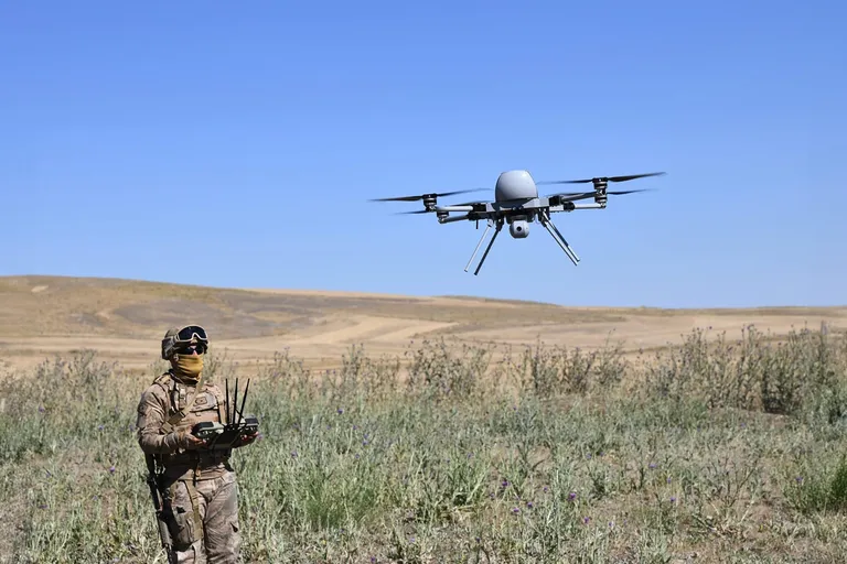 Een geuniformeerde militair bedient een drone die enkele meters voor hem in de lucht hangt.