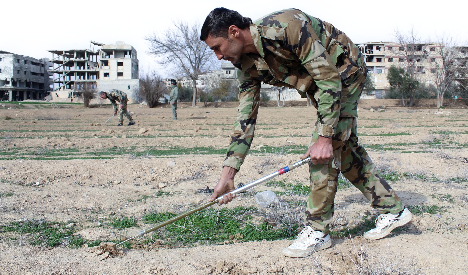 Een Syrische soldaat controleert een open terrein op anti-persoonsmijnen