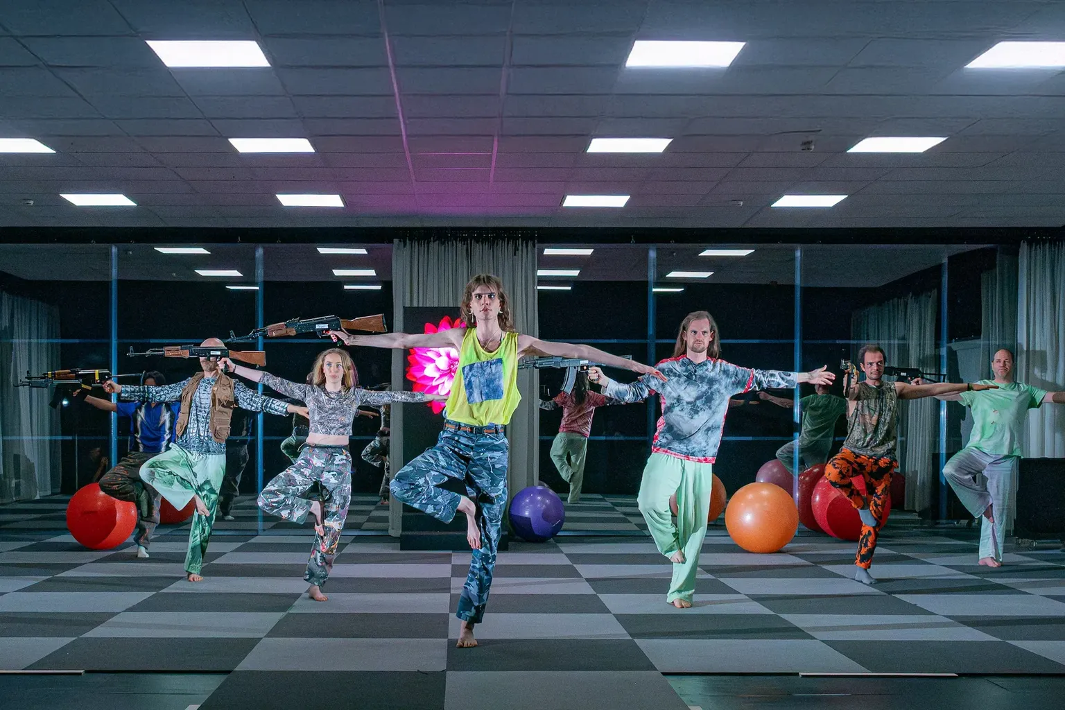 Een groep dansers staat op een been met in de rechterhand een kalashnikov