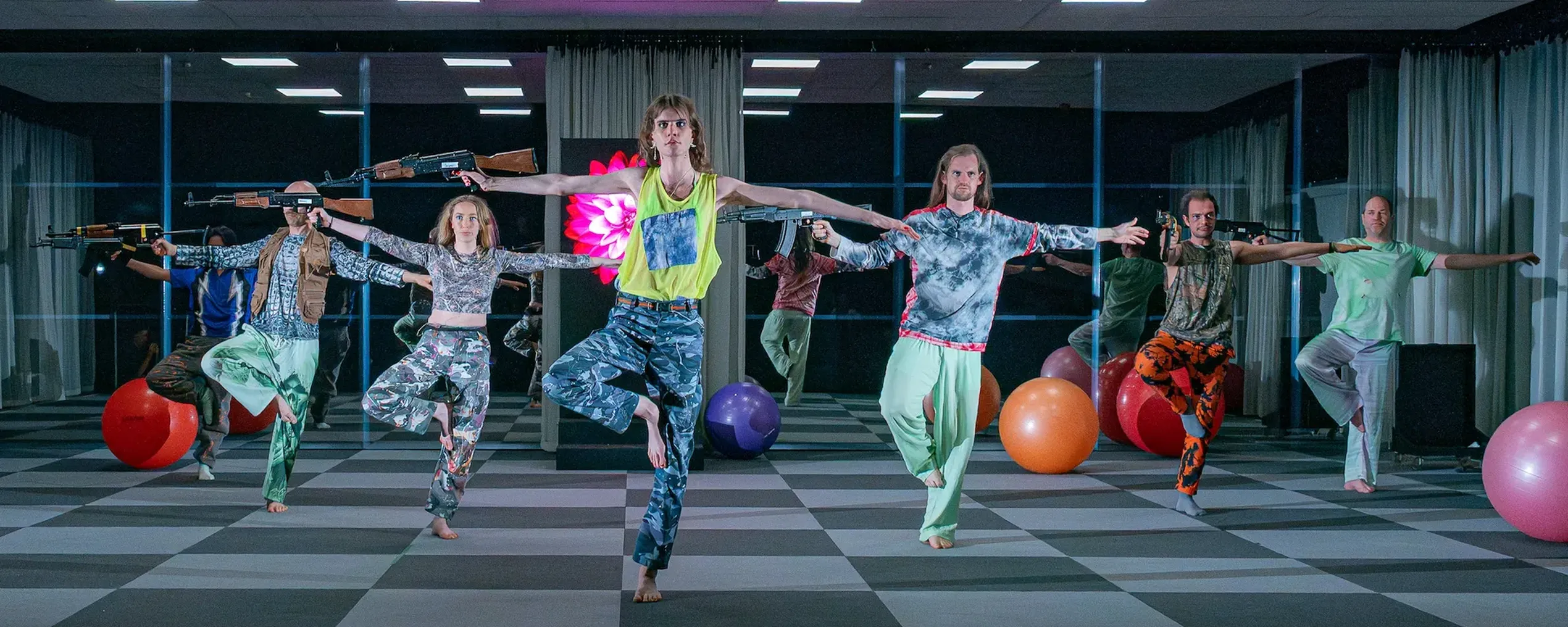 Een groep dansers staat op een been met in de rechterhand een kalashnikov