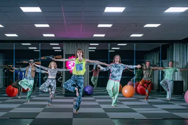 Een groep dansers staat op een been met in de rechterhand een kalashnikov
