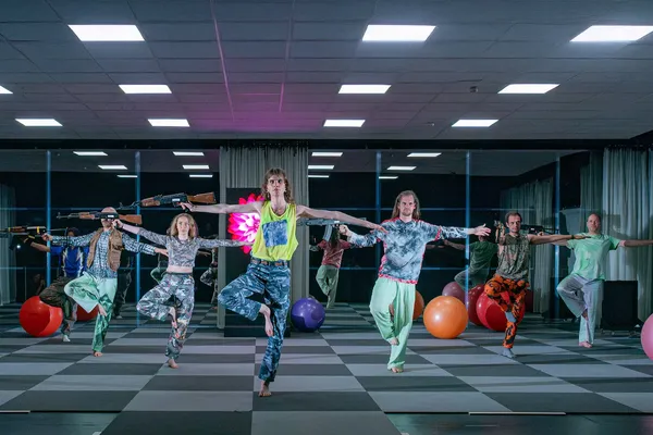 Een groep dansers staat op een been met in de rechterhand een kalashnikov