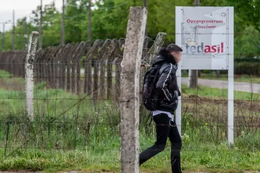 Een man verlaat een met prokkeldraad omgeven terrein en wandelt voobij een bord waarop de vermelding 'Opvangcentrum Broechem, en fedasil staat.
