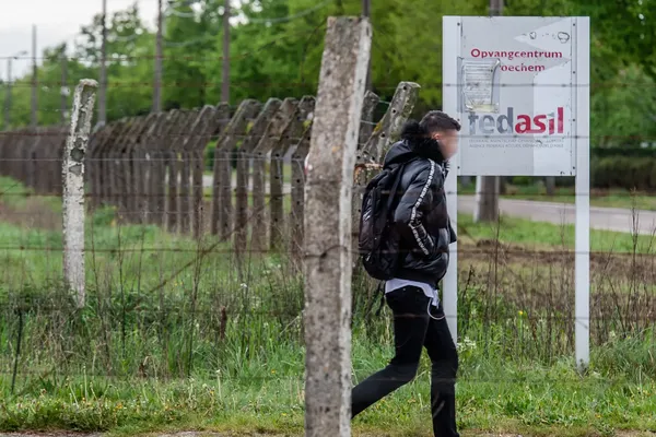 Een man verlaat een met prokkeldraad omgeven terrein en wandelt voobij een bord waarop de vermelding 'Opvangcentrum Broechem, en fedasil staat.