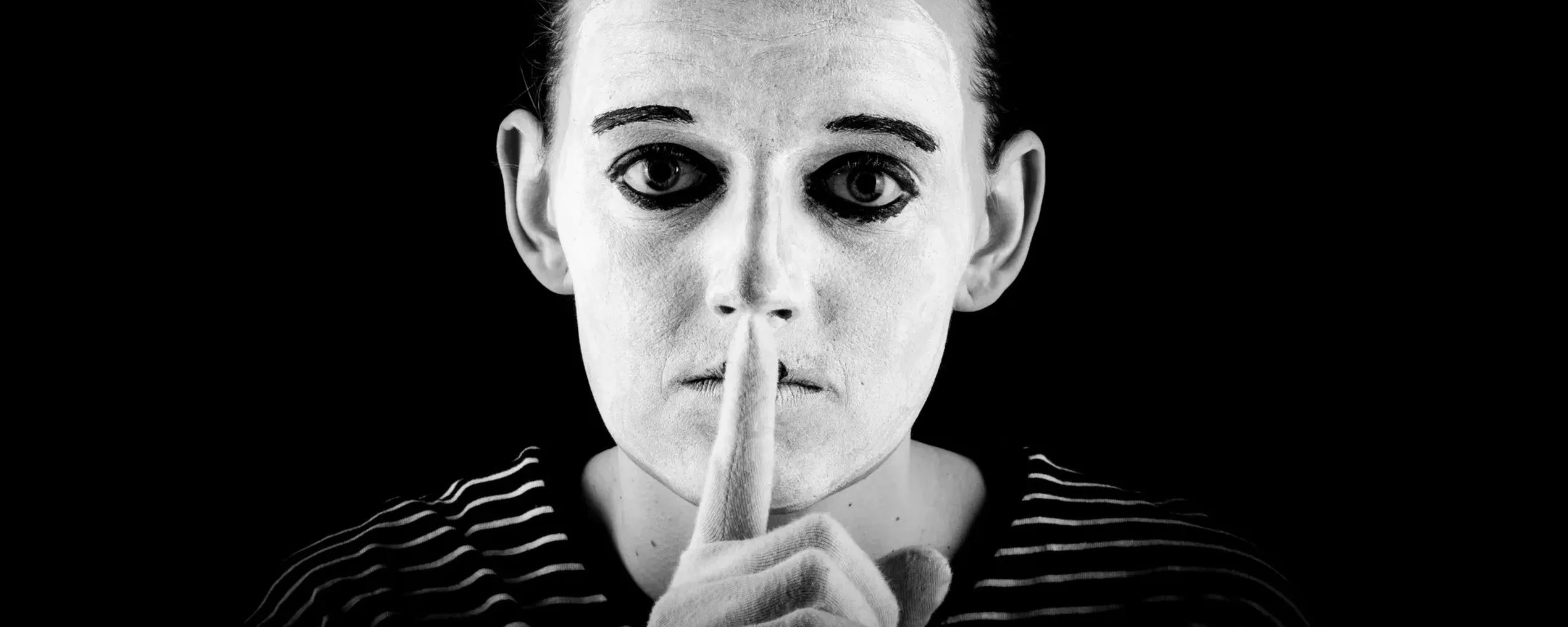 een witgeschminkte mime-speler houdt een wijsvinger voor zijn mond