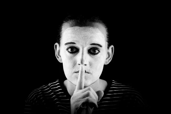 een witgeschminkte mime-speler houdt een wijsvinger voor zijn mond
