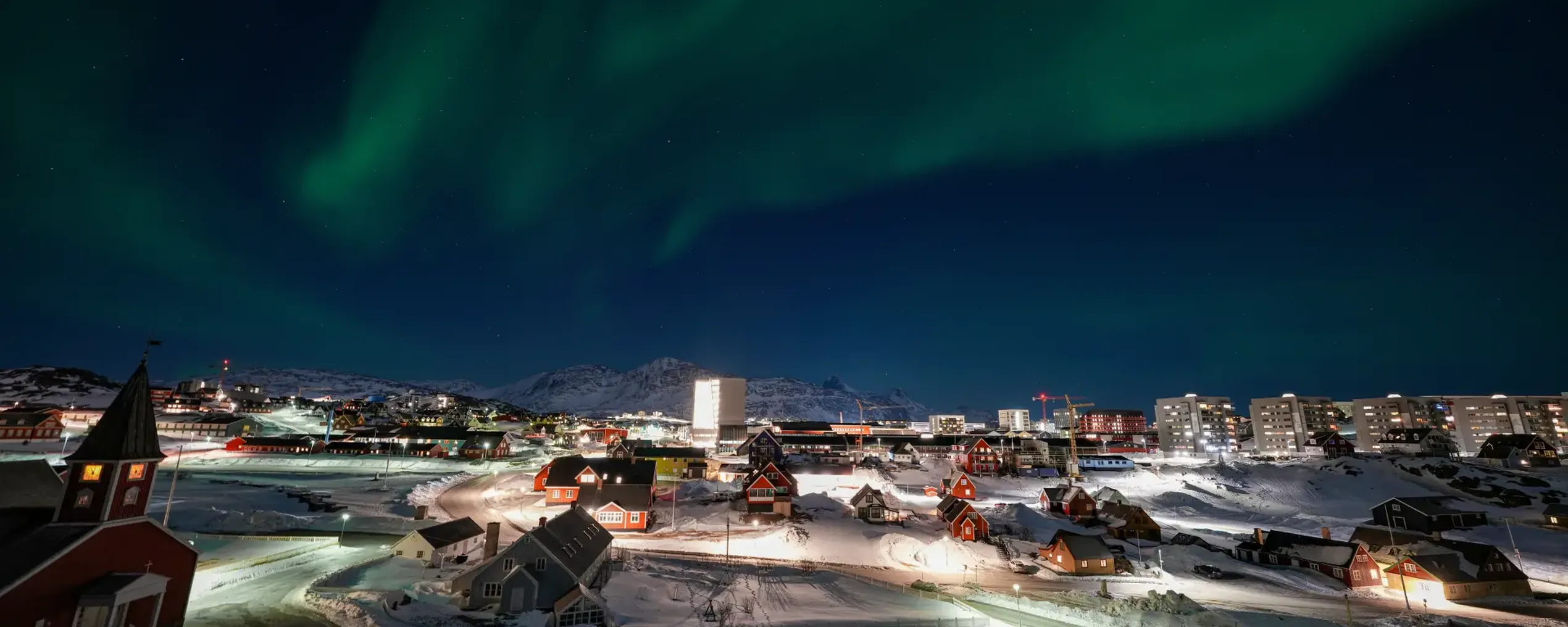Nachtelijk zicht op Nuuk, de hoofdstad van Groenland. In de hemel is Noorderlicht te zien.