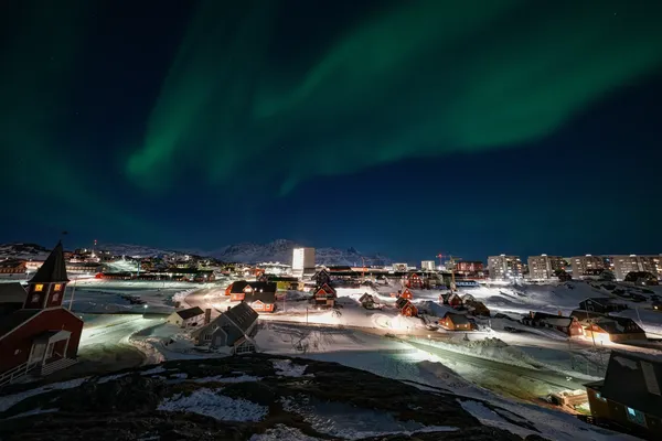 Nachtelijk zicht op Nuuk, de hoofdstad van Groenland. In de hemel is Noorderlicht te zien.