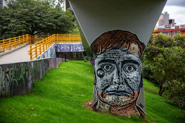Het graffitiportret op de voorgrond stelt El Embolador voor, een personage van de Colombiaanse komiek, journalist, enfant terrible en vredesambassadeur Jaime Garzón. Met El Embolador zette hij politici geregeld in hun hemd. Garzón werd in 1999 op straat doodgeschoten door een paramilitaire militant, waarschijnlijk in opdracht van het Colombiaanse leger.