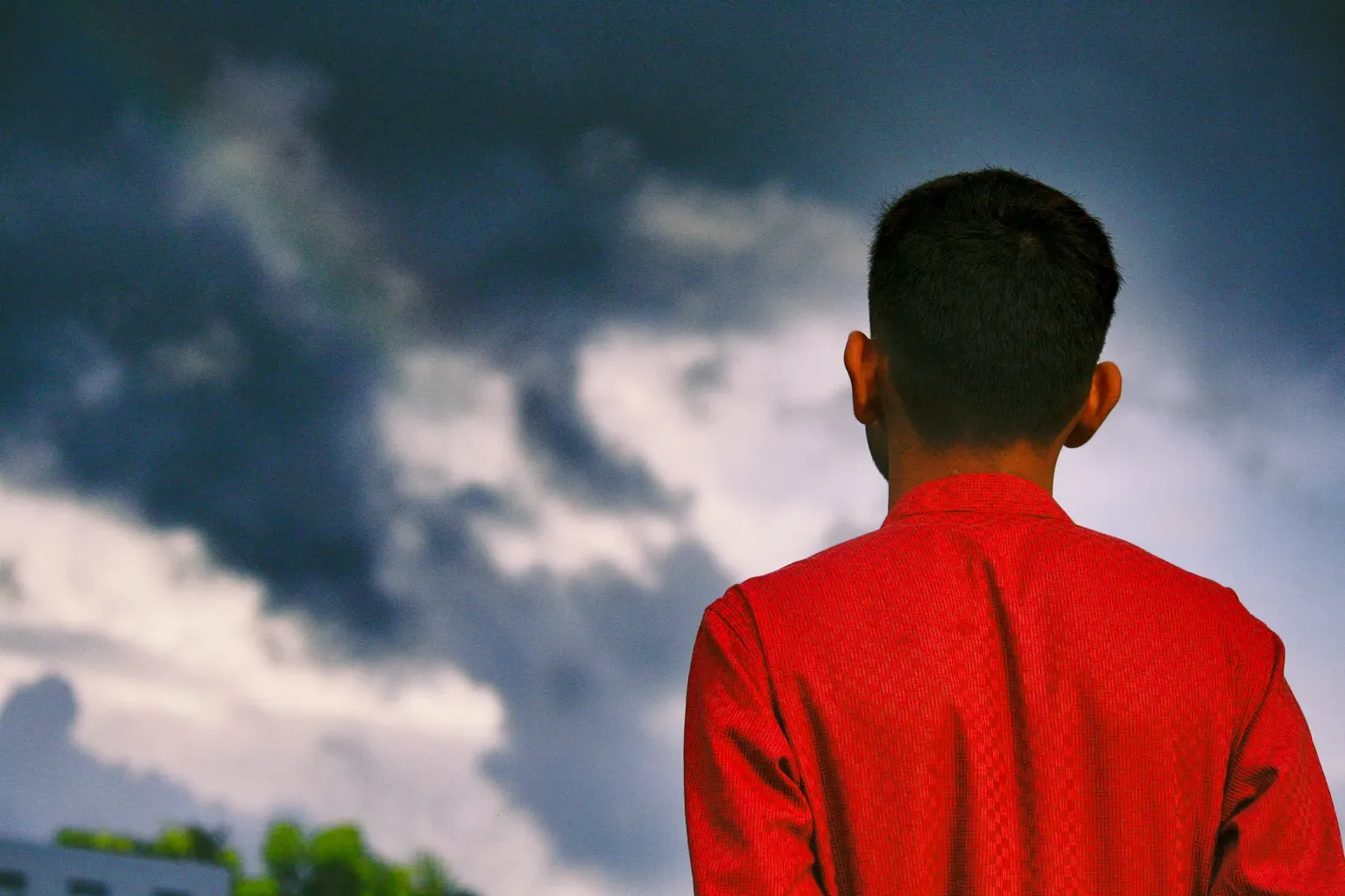 Achteraanzicht van een man in een rood hemd, kijkend naar wolken