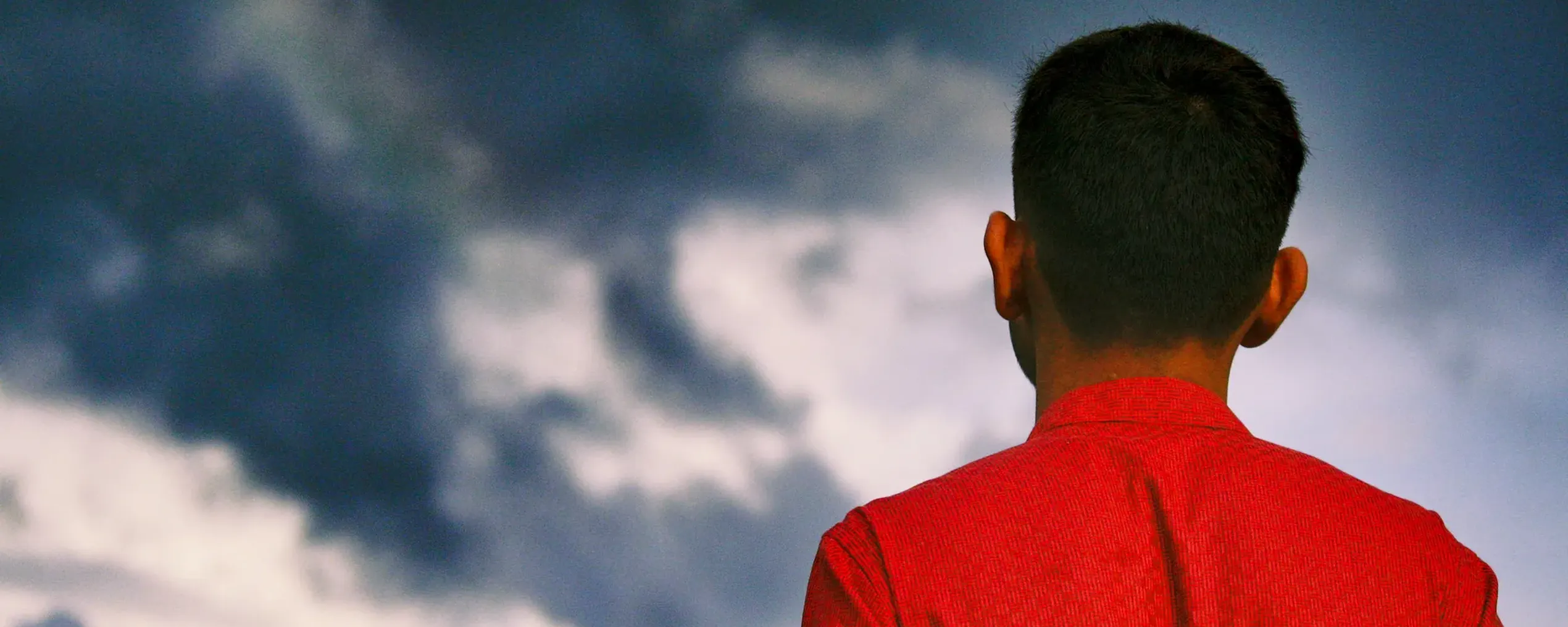 Achteraanzicht van een man in een rood hemd, kijkend naar wolken