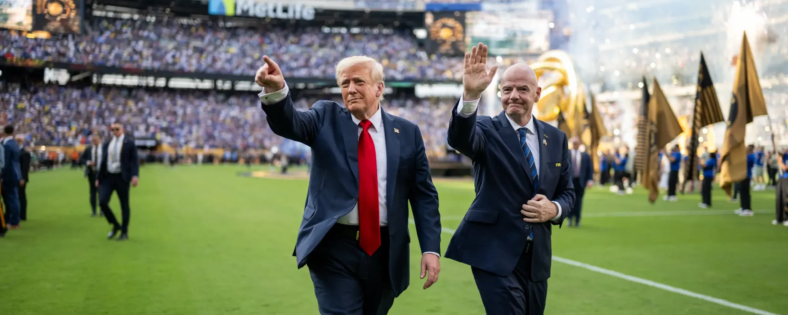 De aerikaanse president Trump en FIFA-voorzitter Gianni Infantino zwaaien naar supporters terwijl ze over een voetbalveld wandelen