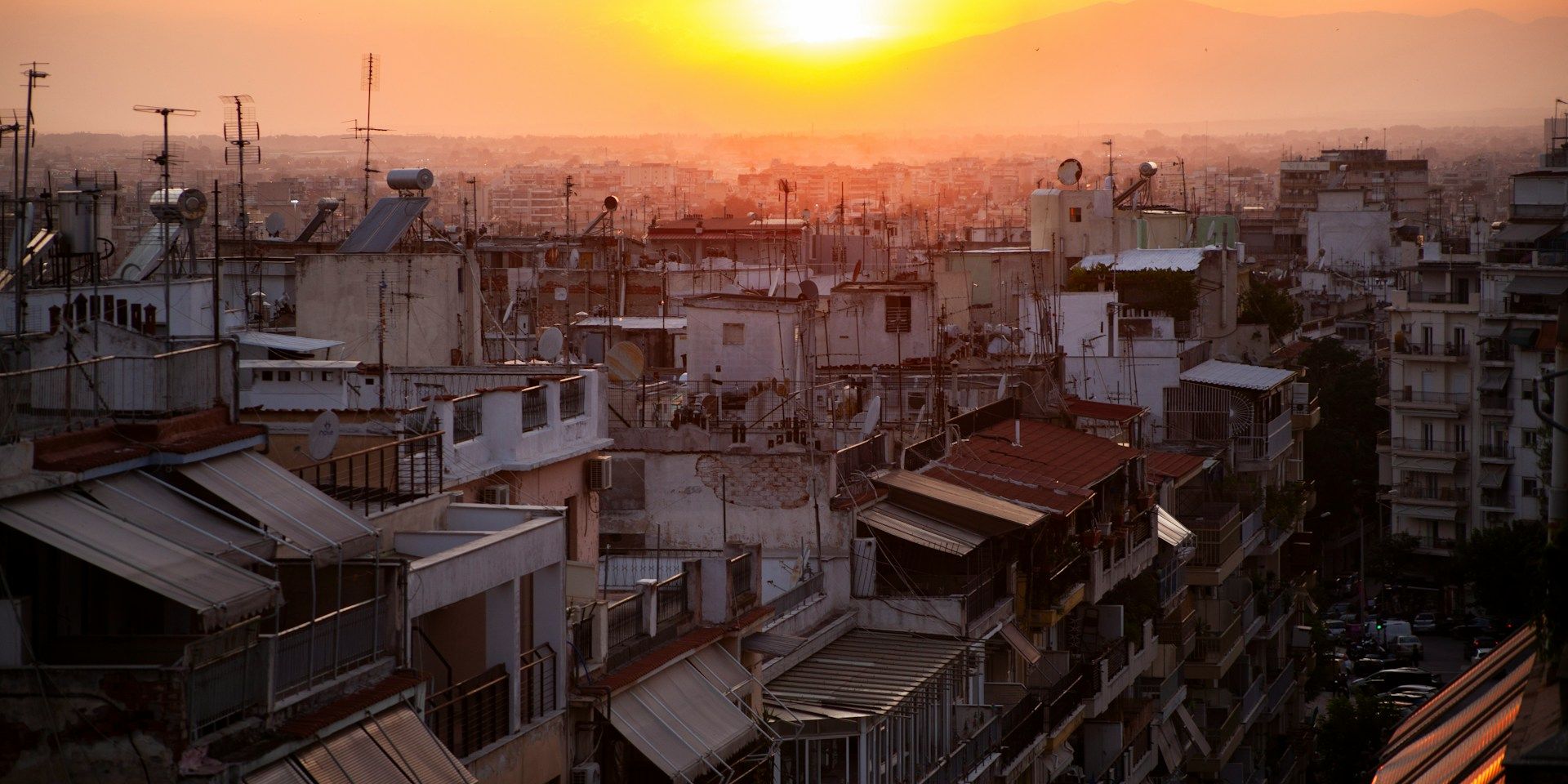 Sunset over a cityscape with densely packed buildings and a vibrant orange sky, casting a warm glow over the urban landscape.