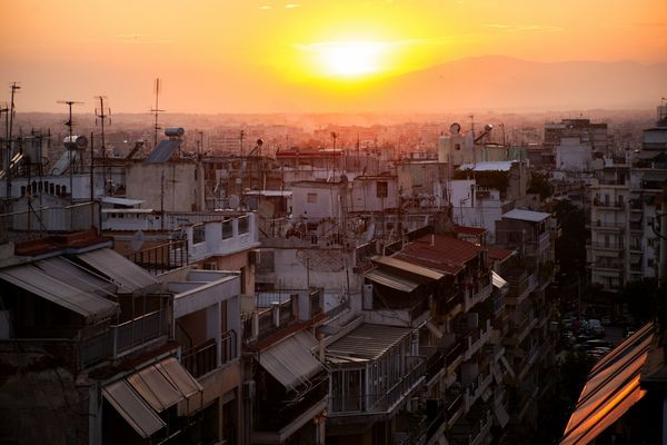 Sunset over a cityscape with densely packed buildings and a vibrant orange sky, casting a warm glow over the urban landscape.