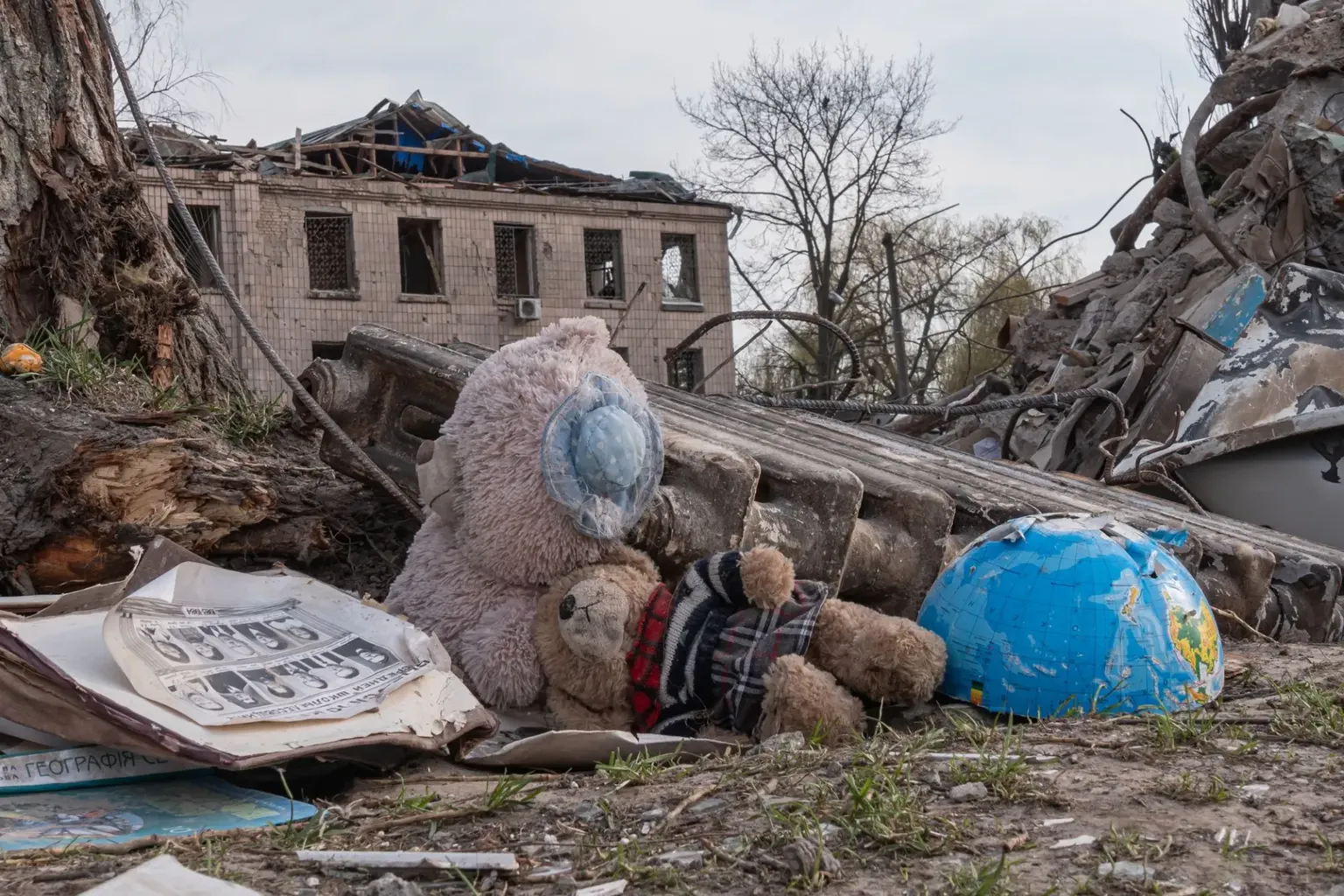 Een halve wereldbol, twee teddyberen, een radiator en een fotoreeks met vermiste personen (?) liggen in het puin voor een vernield huis