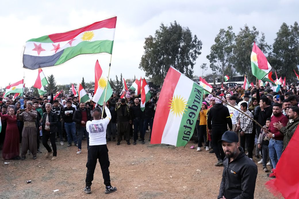 Syrische Koerden zwaaien met een Koerdische en Syrische vlag tijdens een feest voor Newroz