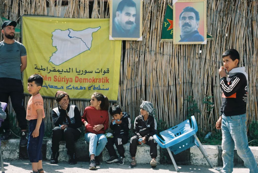 Kinderen zitten voor een vlag van de SDF en portretten van Abdullah Öcalan in Noordoost-Syrië