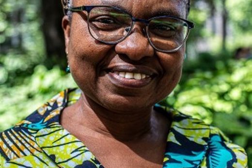 A person wearing glasses and a colorful shirt smiles outdoors, with a blurred green leafy background.