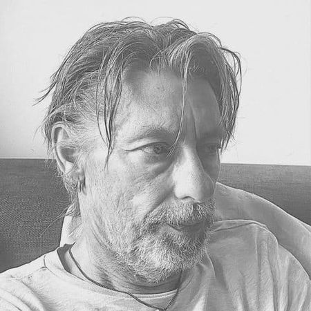 Black and white portrait of a man with a beard and tousled hair, wearing a light shirt, looking contemplatively to the side.