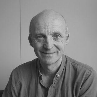Black and white portrait of a smiling bald man in a button-up shirt, with a neutral background.