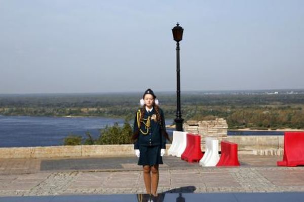 A person in a formal uniform stands on a scenic overlook with a vast view of a river, trees, and distant landscape under a clear sky.