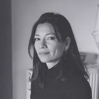 Black and white portrait of a woman with long dark hair, wearing a dark turtleneck, looking at the camera with a neutral expression.