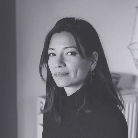 Black and white portrait of a woman with long dark hair, wearing a dark turtleneck, looking at the camera with a neutral expression.