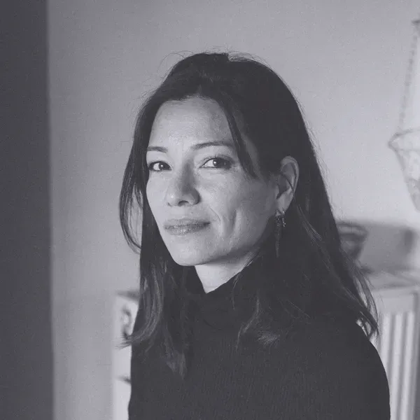 Black and white portrait of a woman with long dark hair, wearing a dark turtleneck, looking at the camera with a neutral expression.