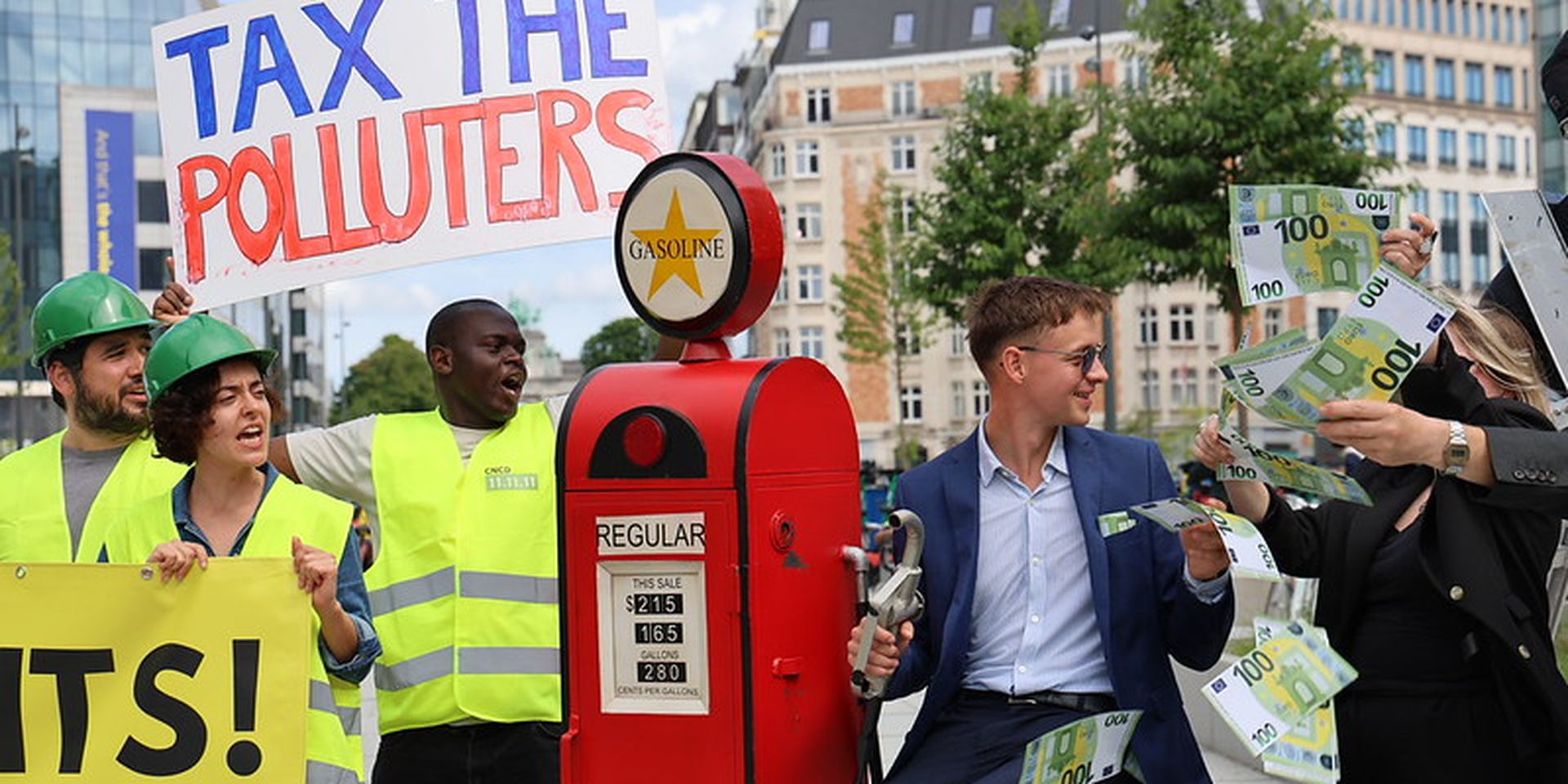 Protesters with signs saying "Tax the Polluters" and "Paris Agreement" confront a well-dressed man holding money by a gasoline pump.