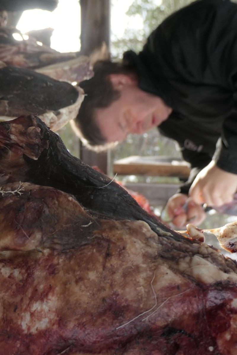 Person preparing meat in a cold, outdoor setting, surrounded by hanging pieces.