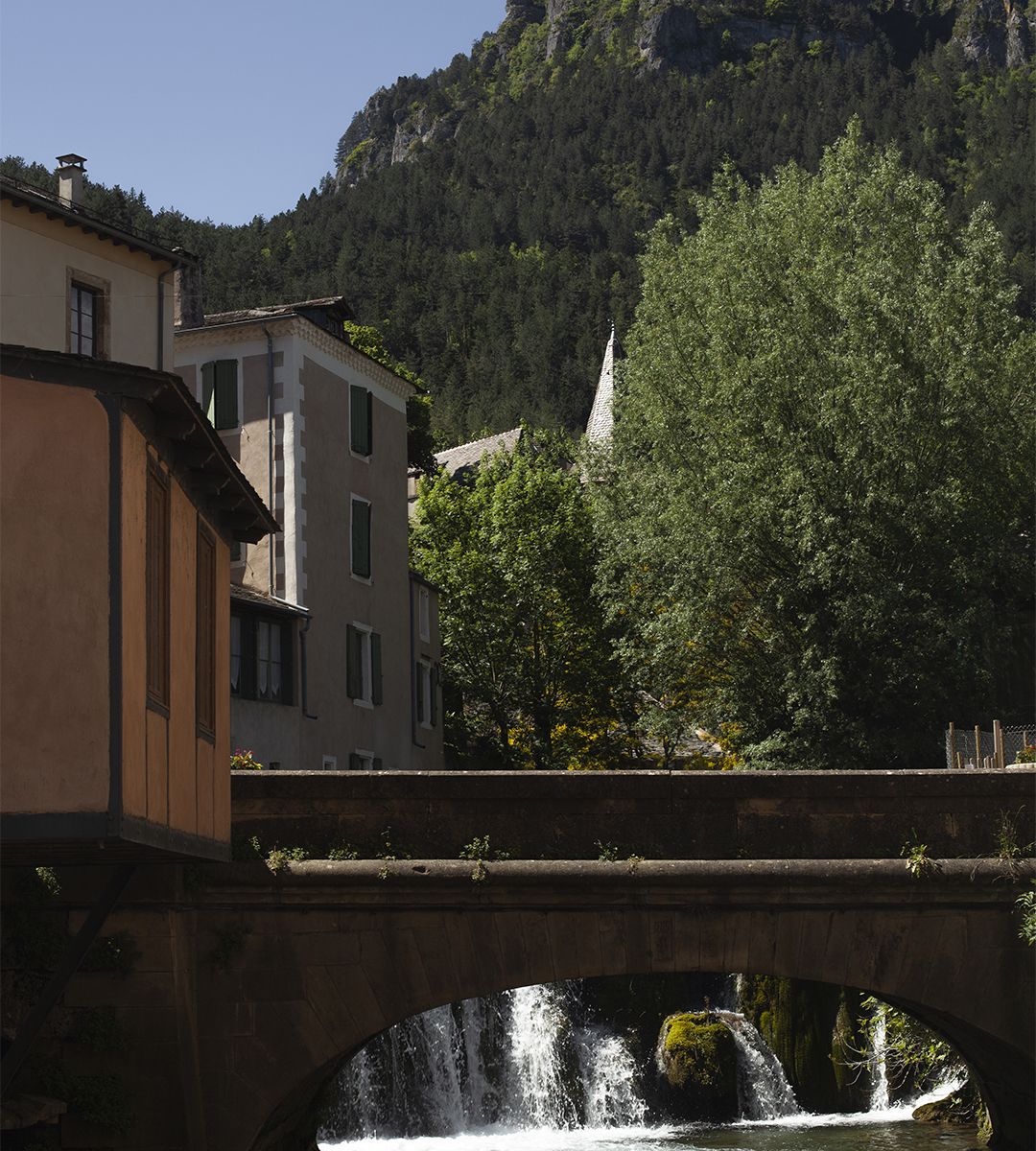 Pont en pierre avec cascade et maisons d’un village cévenol en arrière-plan | Atelier Tuffery