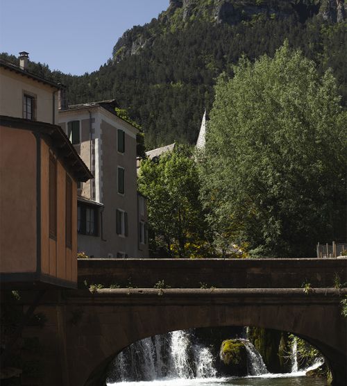 Pont en pierre avec cascade et maisons d’un village cévenol en arrière-plan - Atelier Tuffery