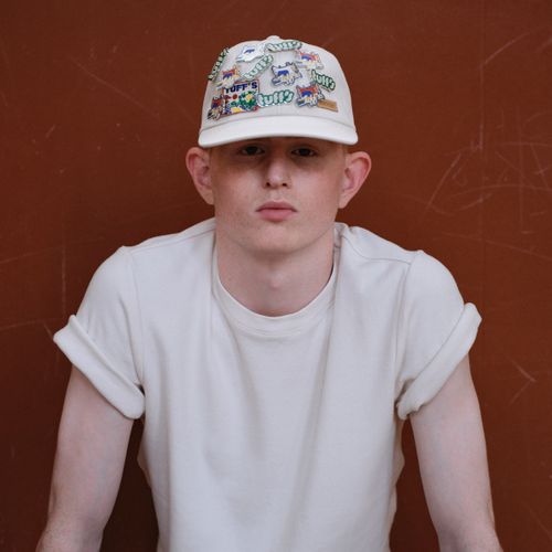 Homme avec un t-shirt écru qui porte une casquette écrue avec des pins Tuff's et patch vintage - Atelier Tuffery