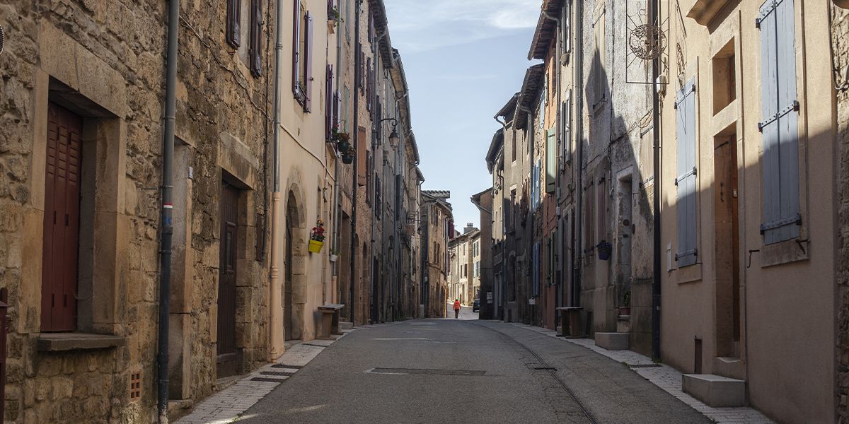 Rue pavée d’un village cévenol, bordée de maisons en pierre et volets colorés | Atelier Tuffery