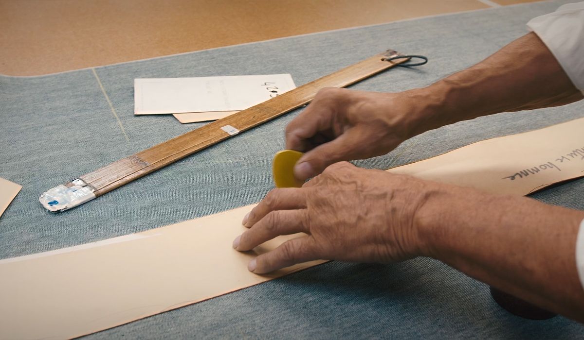 Des mains dessinent sur de denim avec un craie, entourées d’une règle et de gabarits en papier. | Atelier Tuffery