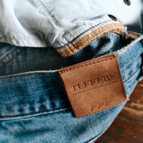 Détail du patch en cuir Atelier Tuffery cousu sur un jean posé sur une table. - Atelier Tuffery