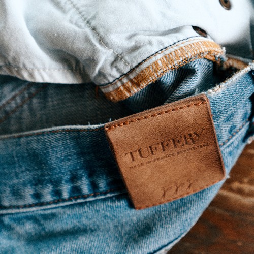 Détail du patch en cuir Atelier Tuffery cousu sur un jean posé sur une table. - Atelier TUFFERY